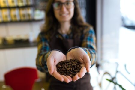 Beautiful young saleswoman holding coffee grains in organic shop