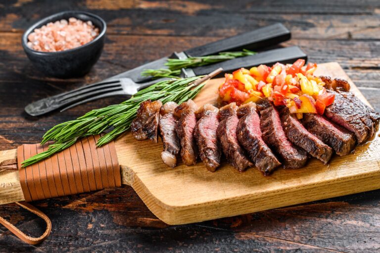 Grilled top sirloin cap or picanha steak on a cutting board with herbs