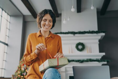 Happy young Spanish woman engaged in packing Xmas gifts at home during Christmas holidays
