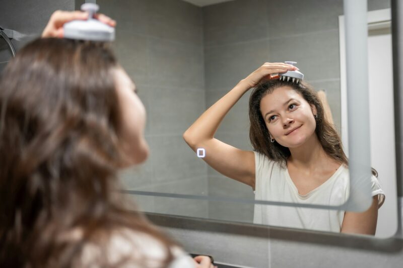 Young woman with dark curly hair doing self hair scalp massage with scalp massager or hair brush for