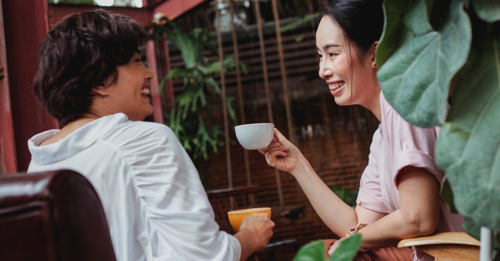 Automatização de pedidos via mensagens instantâneas Duas mulheres sorrindo e se comunicando enquanto tomam café em um ambiente aconchegante.