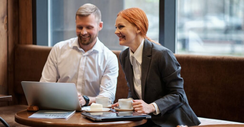 Um homem e uma mulher sorrindo enquanto trabalham em um laptop, com xícaras de café na mesa.