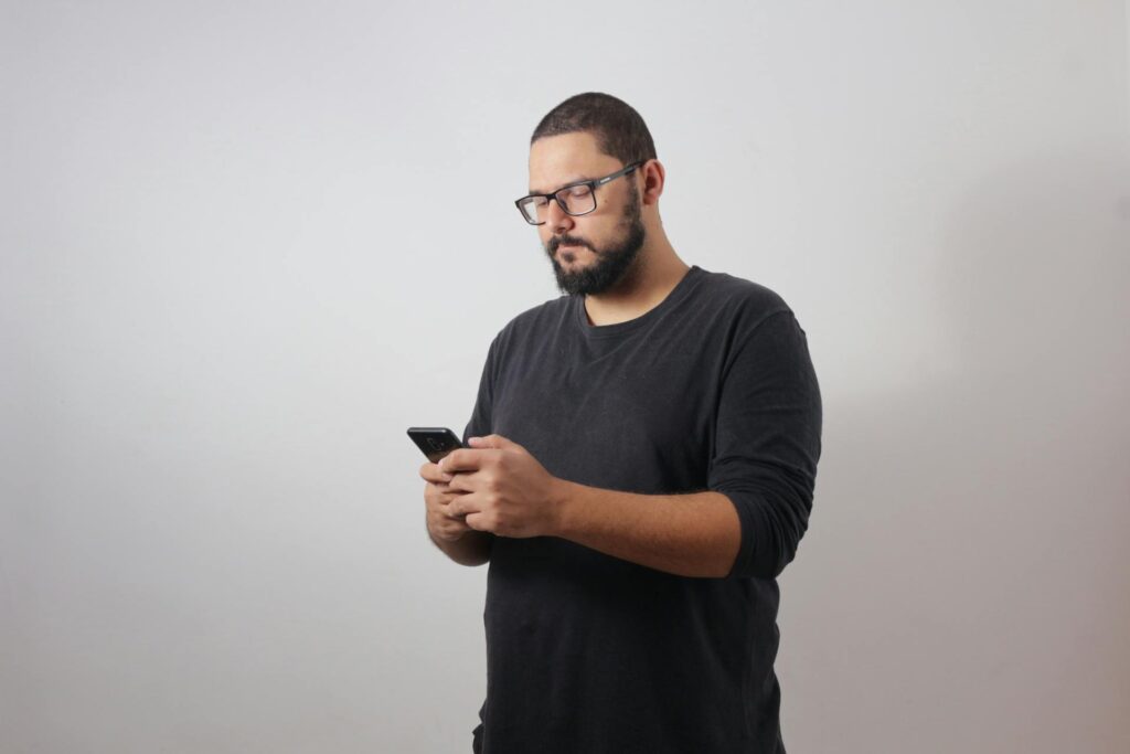 Dicas para evitar erros ao salvar vídeos da internet Homem em primeiro plano, usando smartphone, com camisa escura.