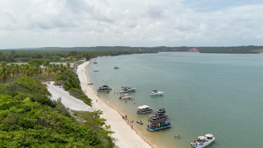 Vista aérea de uma praia com barcos ancorados e pessoas se divertindo na água.