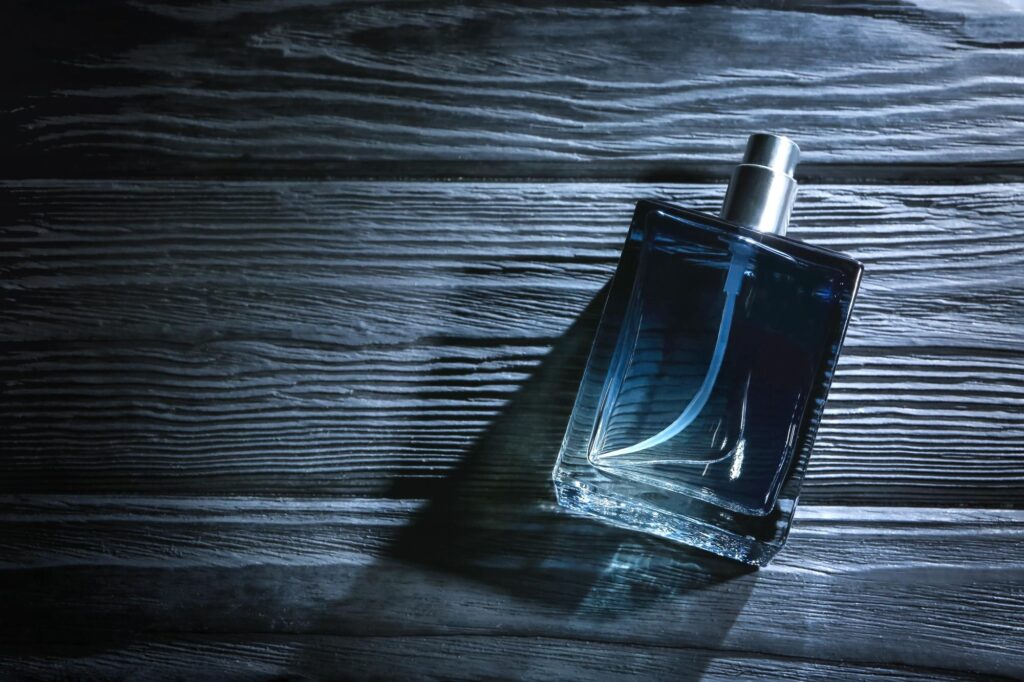 Frasco de perfume masculino em vidro azul sobre fundo de madeira escura iluminado pela luz
