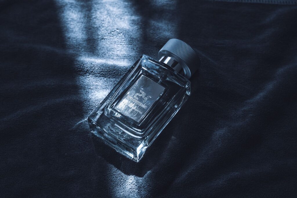 Arbo é perfume masculino ou feminino? A resposta Frasco de perfume masculino de vidro transparente com tampa prateada repousando sobre tecido escuro texturizado