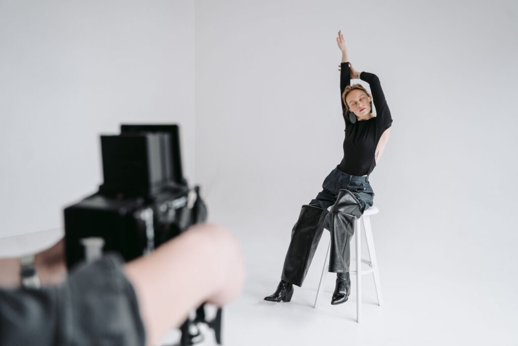 Como se preparar para um ensaio fotográfico feminino Mulher sentada em banqueta branca, com os braços erguidos, posando durante um ensaio fotográfico em estúdio iluminado