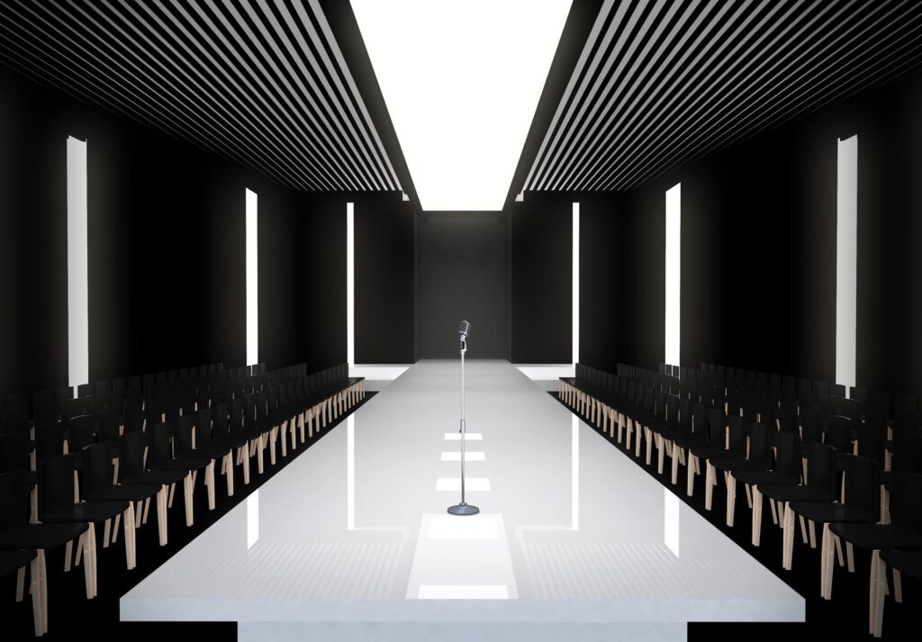 Palco de desfile de moda com microfone e cadeiras pretas em ambiente iluminado